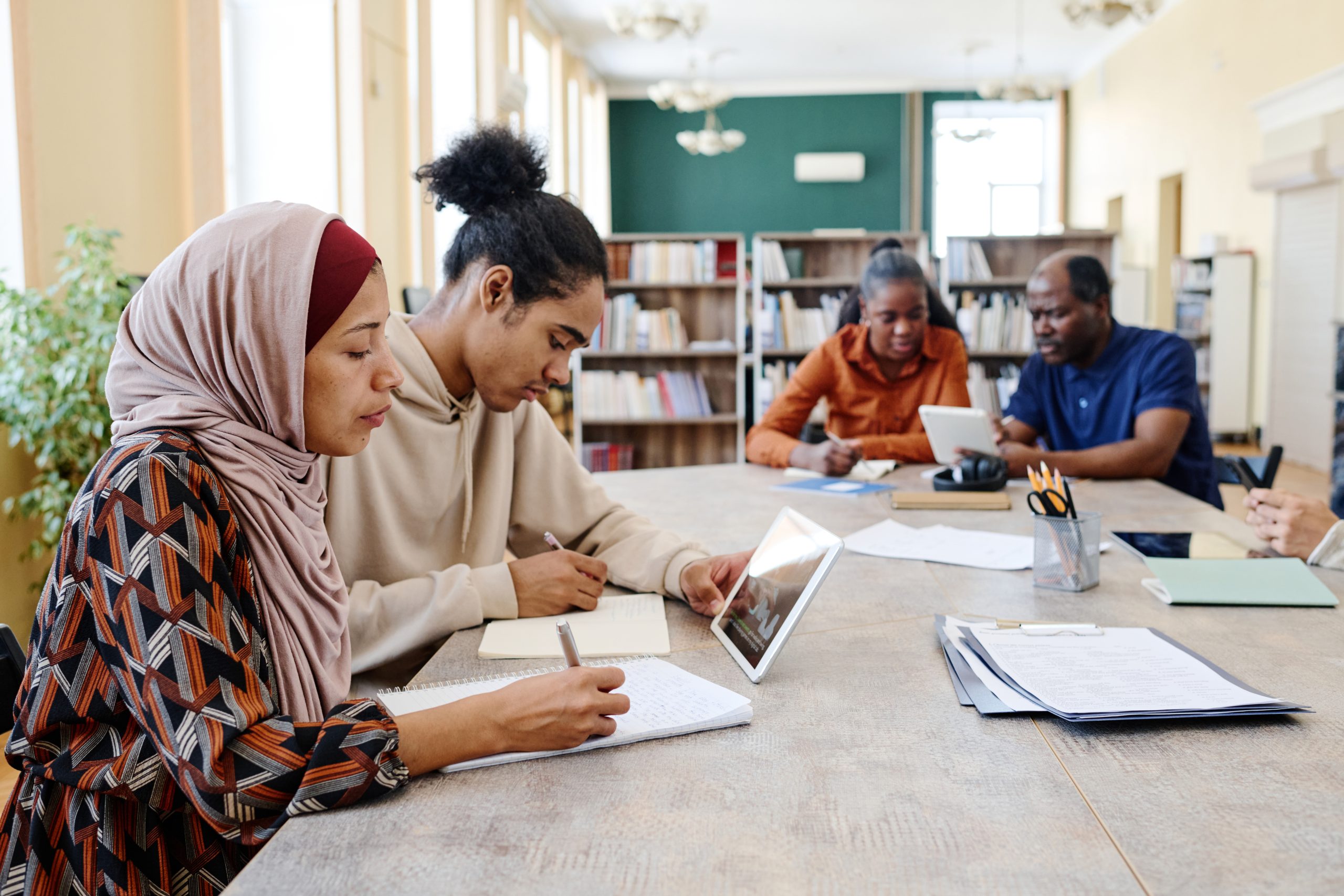 Professores e alunos de diferentes culturas sentados em mesa de estudos